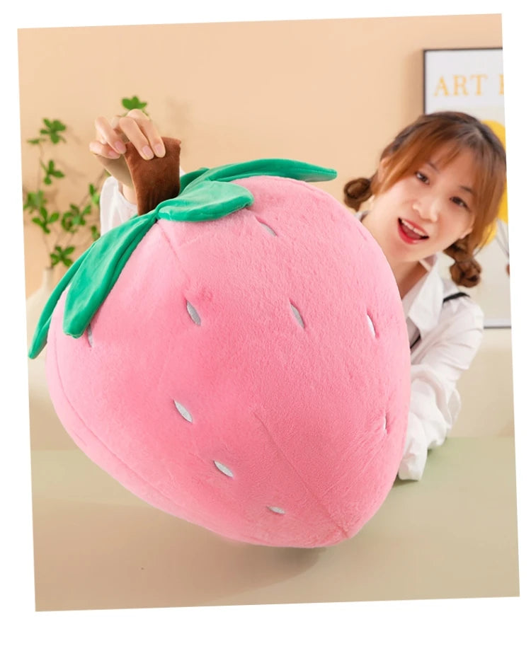 A pink strawberry plush throw pillow with green leaves is being held by a woman.