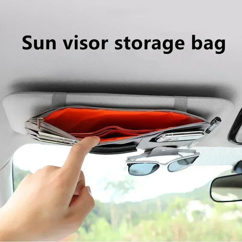 A hand is opening a storage bag for a sun visor in a car, showing the interior organization.