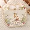 A light yellow baby bib featuring a giraffe and a duck in a floral pattern, displayed on a white surface.