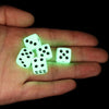 A hand holds a set of glow-in-the-dark acrylic dice on a dark background.