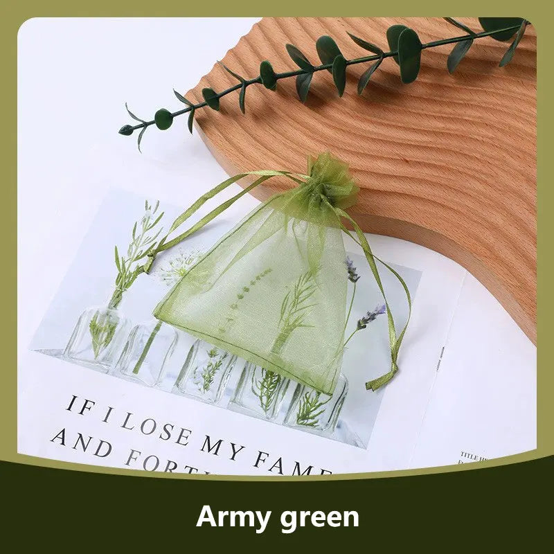 Army green organza drawstring jewelry gift bags with dried greenery displayed on a wooden surface.