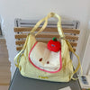 A yellow nylon messenger bag with a strawberry charm is displayed on a wooden shelf.