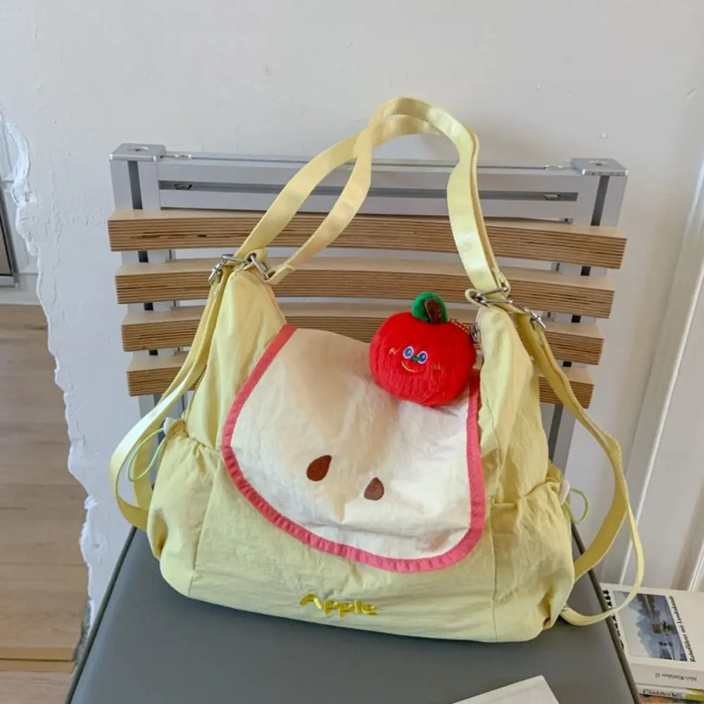A yellow nylon messenger bag with a strawberry charm is displayed on a wooden shelf.