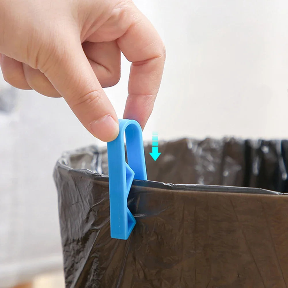 A hand is using a blue clip to secure a garbage bag onto the rim of a dark trash can.