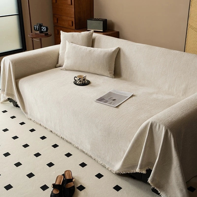 A cream-colored chenille sofa with tassel edges and pillows, draped on a light rug.
