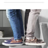 A pair of brown and gray leather shoes are placed on a modern white stool in front of a toilet.