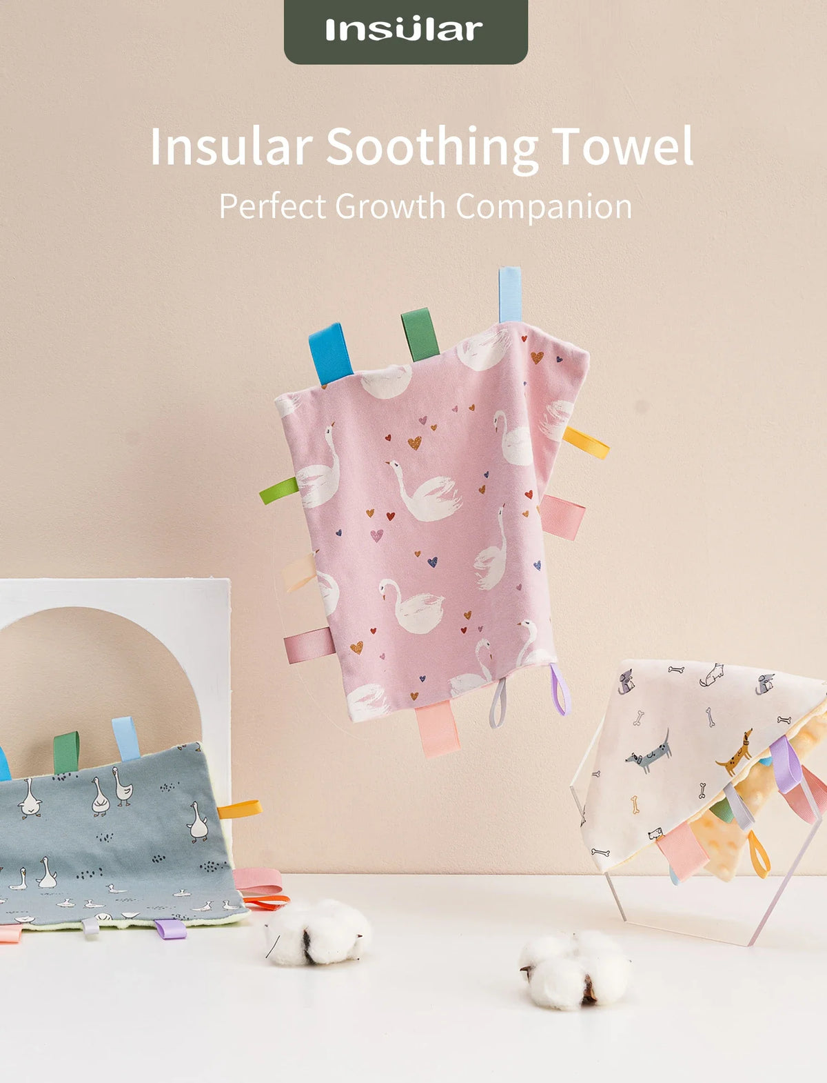 A pink baby sensory tag comfort blanket with white swan designs and a soothing teether hanging on a wall.