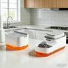 A white countertop soap dispenser with an orange base and a built-in sponge holder sits on a white kitchen counter.