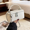 A white quilted woven leather crossbody bag with silver chain details being held by a hand in a bright room.