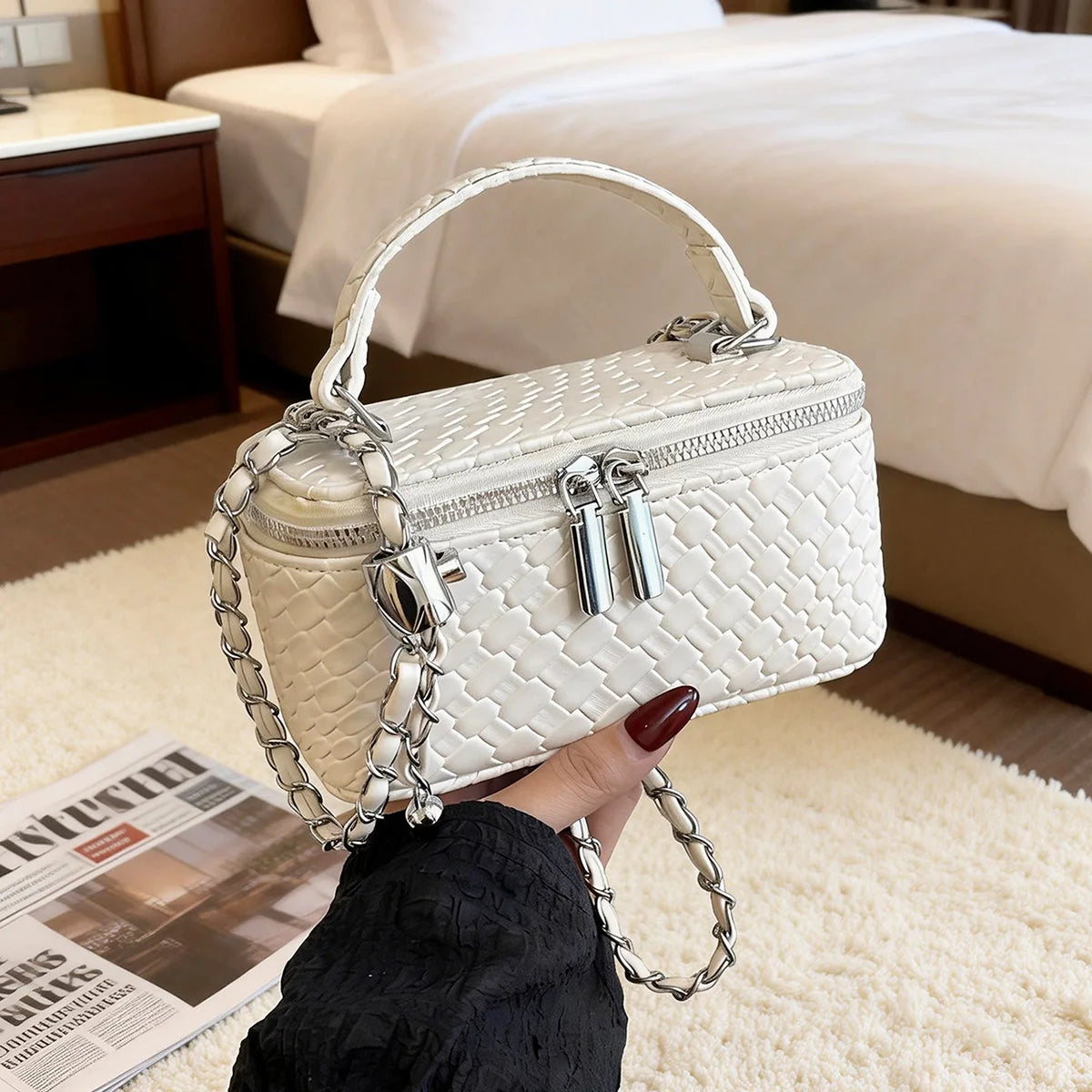 A white quilted woven leather crossbody bag with silver chain details being held by a hand in a bright room.