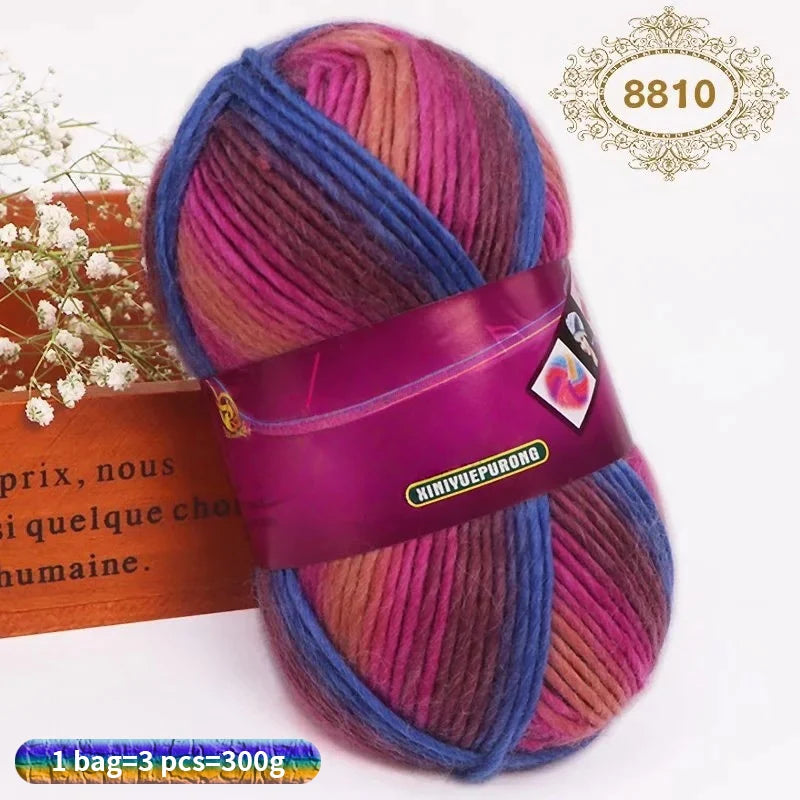 A ball of gradient dyed wool blend yarn in shades of pink, purple, and blue, tied with a purple ribbon.