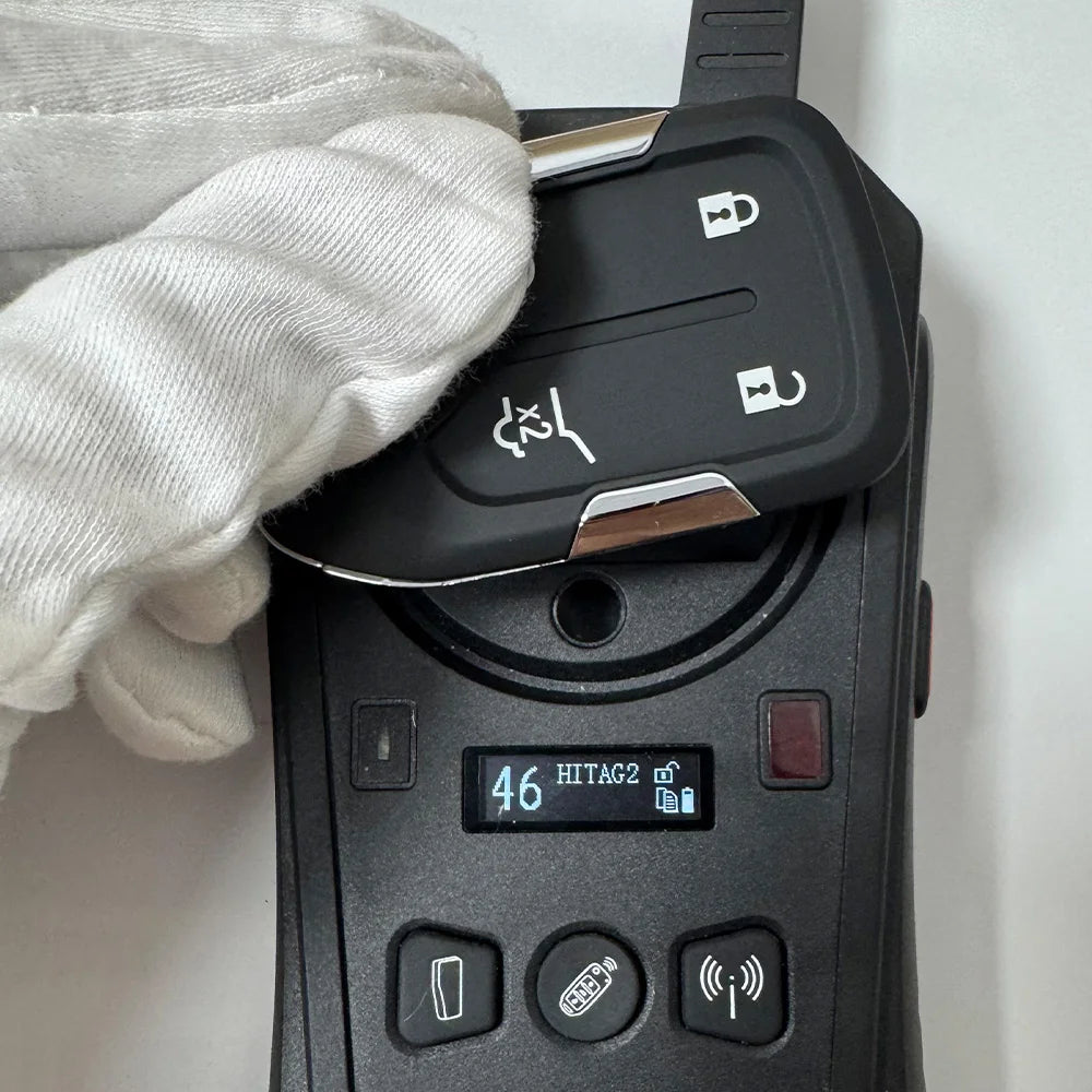 A hand wearing a white glove holds a black replacement remote key for a vehicle.