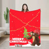 A red flannel throw blanket featuring a Christmas theme with lights, a green tree, and a brown bear.