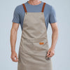 A man wearing a beige waterproof kitchen apron over a blue t-shirt and olive green pants.