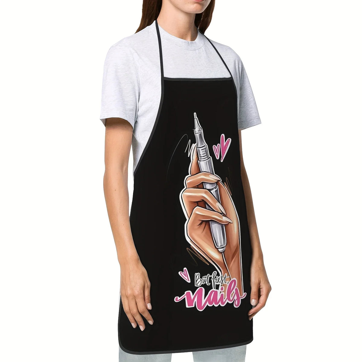 A woman wearing a black apron over a gray t-shirt, featuring a hand painting nails on the apron.