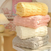 A stack of fluffy coral pink and cream velvet bath towels displayed on a light wooden surface.