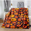 A dark brown flannel throw blanket featuring an orange pumpkin print, displayed on a white sofa.