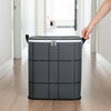 Eine Hand hebt eine graue Stofftasche mit schwarzen Henkeln in einem Flur.