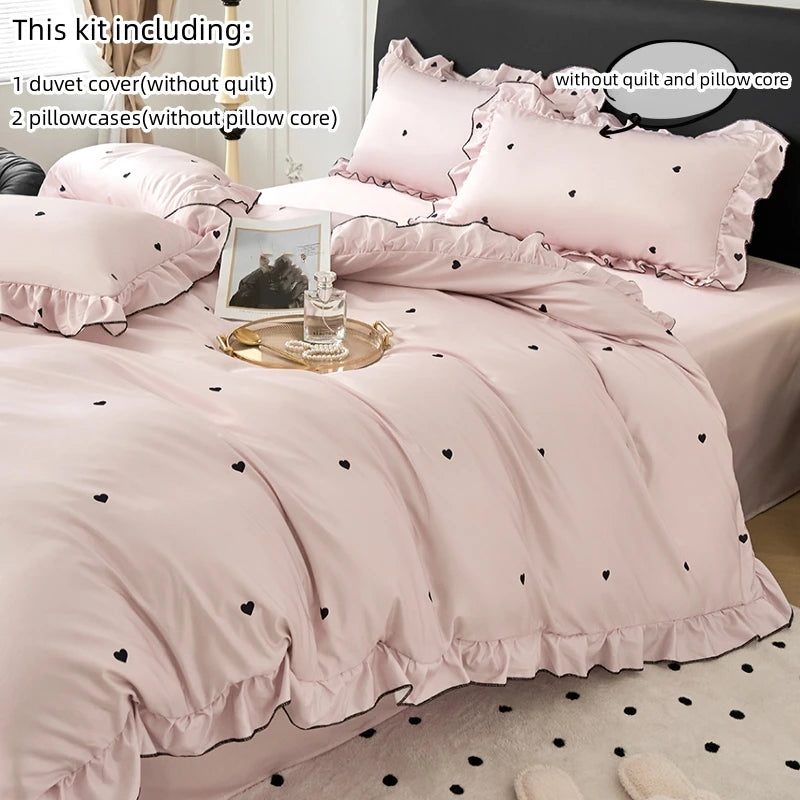 A pink duvet cover set with black heart print and matching pillowcases shown on a bed.