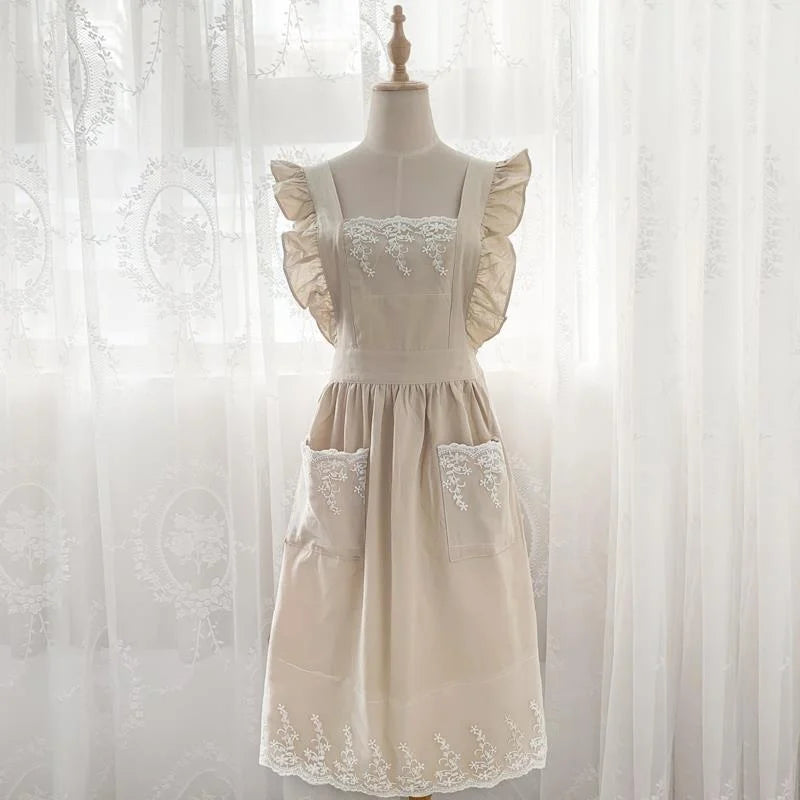 A cream-colored kitchen apron made of cotton linen with lace trim and ruffled sleeves displayed on a mannequin.