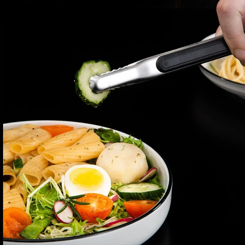 A hand uses premium stainless steel BBQ tongs to lift a slice of cucumber from a bowl of salad.