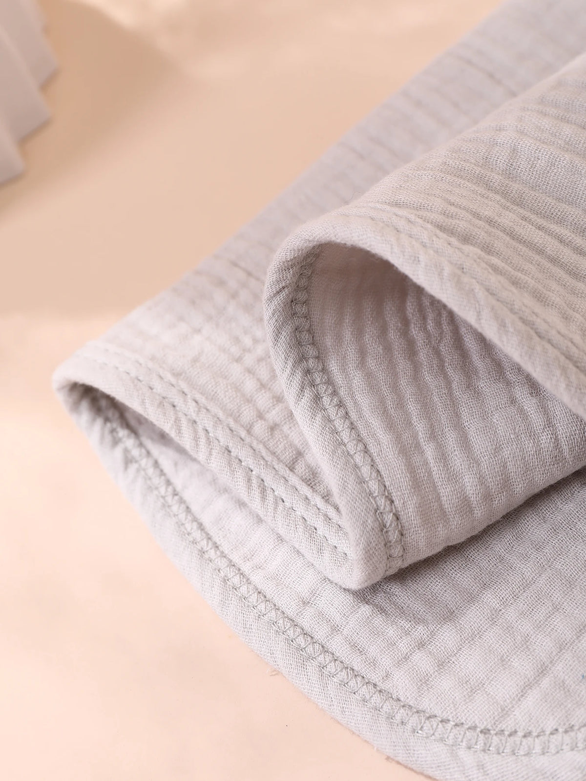 A close-up of a light beige, ribbed baby burp cloth folded and displayed on a soft background.