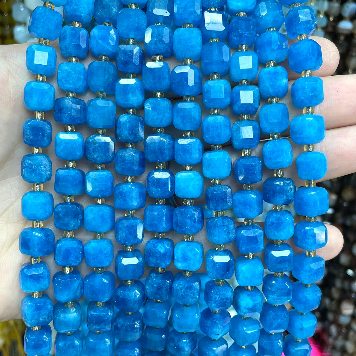 A hand holds a strand of bright blue natural stone square faceted beads for jewelry making.