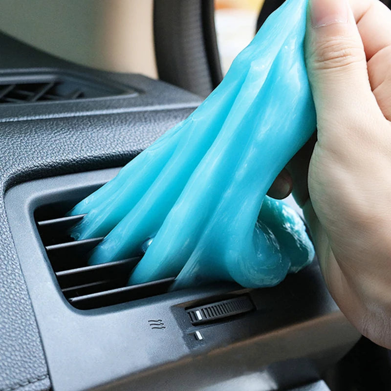 A hand is squeezing a translucent blue reusable cleaning gel for car interiors and electronics into a vent.