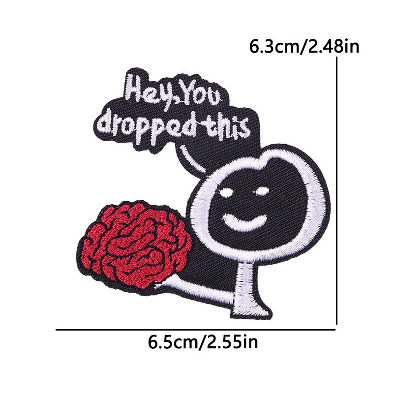 Black embroidered patch featuring a smiling face with a brain, with text saying Hey You dropped this.