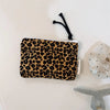 A black leopard print cosmetic bag with a white zipper and a black tassel is displayed on a white surface.