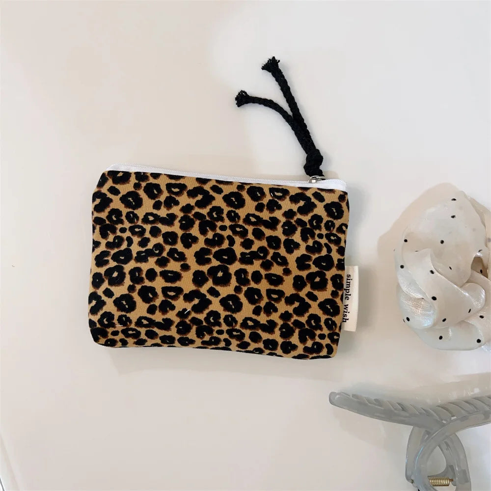 A black leopard print cosmetic bag with a white zipper and a black tassel is displayed on a white surface.