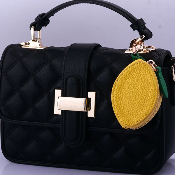 Bolso acolchado negro con herrajes dorados y un llavero de fruta amarilla.