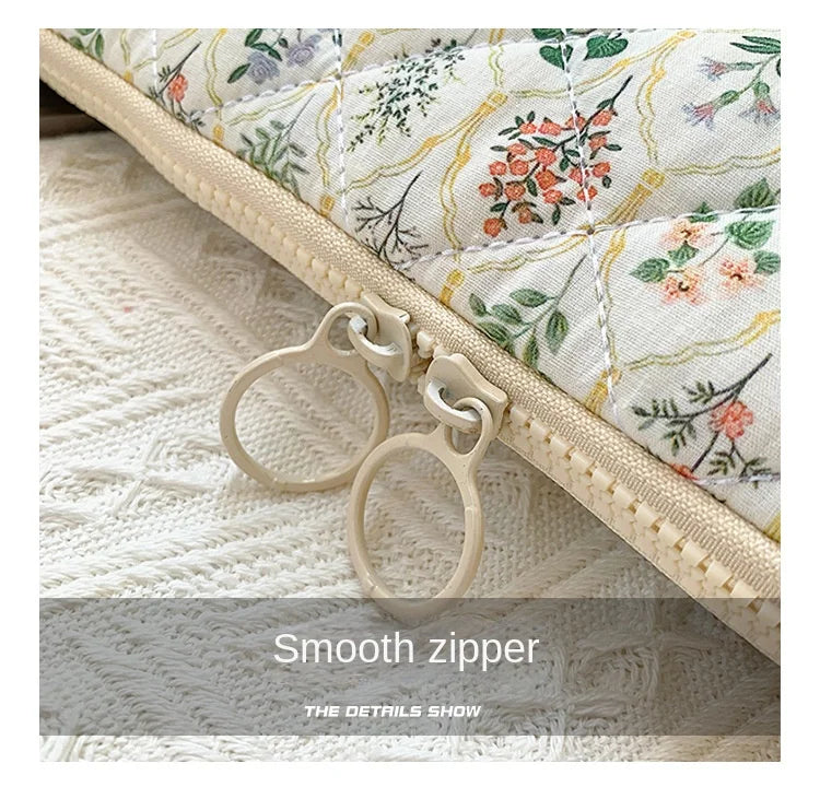 Close-up of a floral printed fabric laptop sleeve featuring a smooth zipper closure on a beige quilted edge.