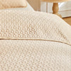 A beige quilted bedspread and matching pillow shams are shown on a bed.