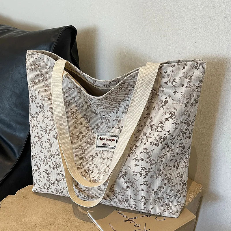 A beige corduroy tote bag with a floral pattern resting on a light brown box.