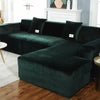 A dark emerald green plush velvet elastic sofa cover draped over an L-shaped sectional in a modern living room.