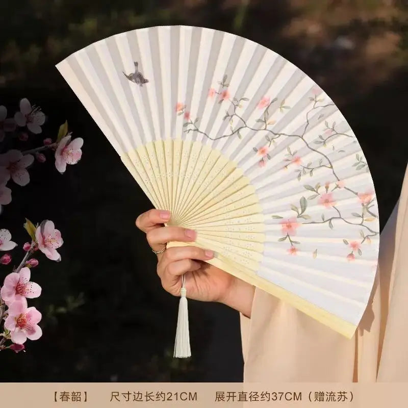 A light gray bamboo and silk folding fan with pink floral designs is being held in a close-up shot.