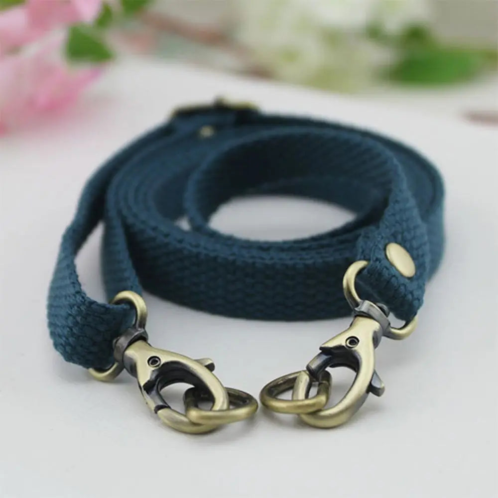 A dark teal canvas shoulder strap with brass hardware is shown against a white background.
