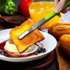 A stainless steel BBQ tong is lifting a piece of grilled bread and butter onto a plate with fruit preserves.