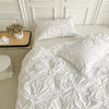 White luxury duvet cover set featuring a quilted pattern with floral pinch-pleats on a bed.