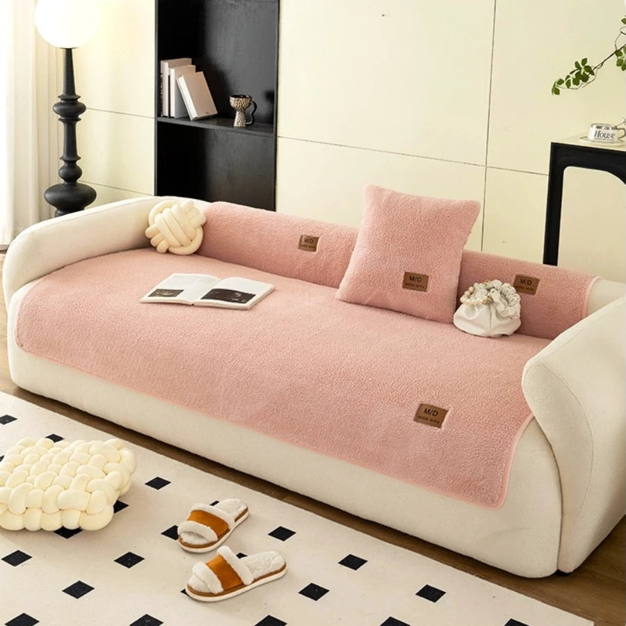 Une housse de canapé sherpa rose est exposée sur un canapé blanc, avec de petits chaussons blancs à proximité.