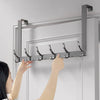 A hand is installing an over-the-door organizer rack with eight hooks onto a white door frame.