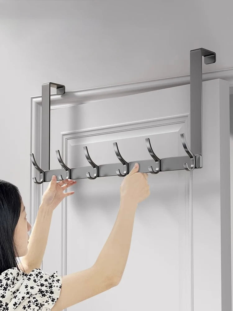 A hand is installing an over-the-door organizer rack with eight hooks onto a white door frame.