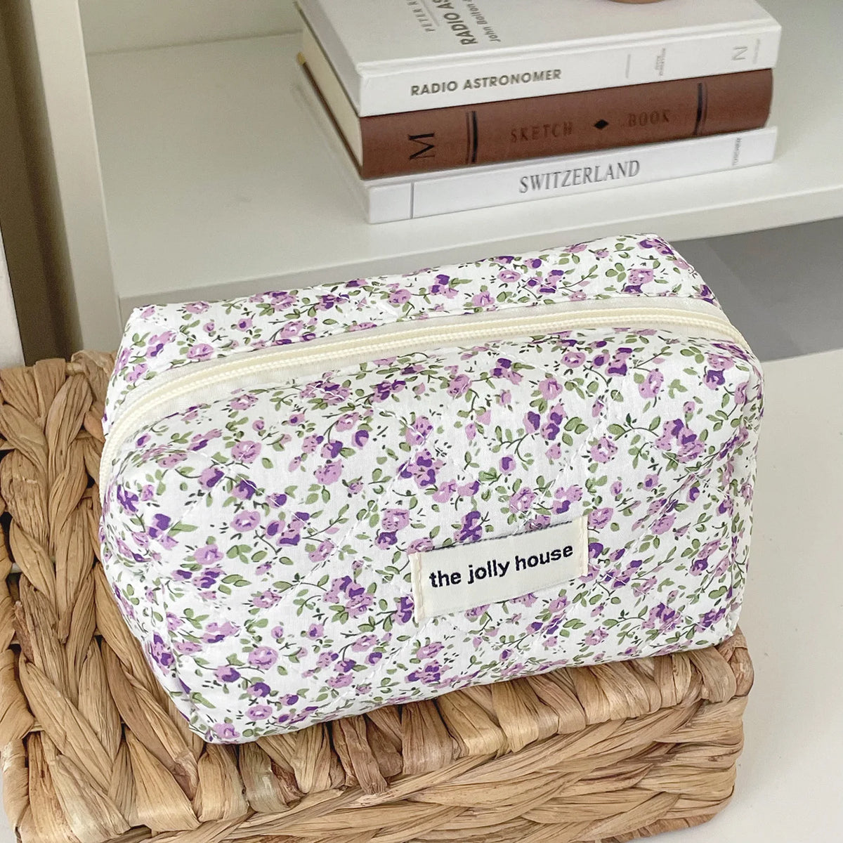 A floral quilted makeup bag with a purple and green pattern resting on a woven tray.