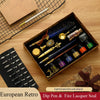 A set of European retro dip pens and fire lacquer seals displayed in an open wooden box on a light wood surface.