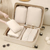 A beige packing cubes set is displayed inside a light-colored storage box with various fabric items and sunglasses nearby.