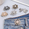 A collection of adjustable flower waist clips in silver and gold tones displayed on a denim fabric.