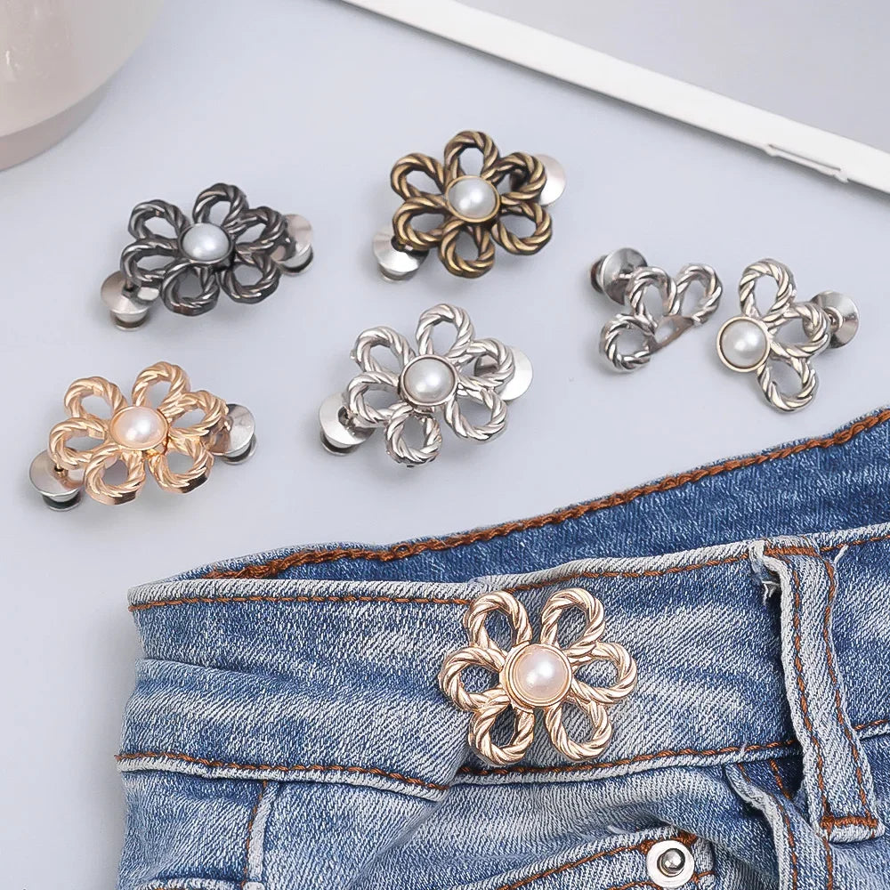A collection of adjustable flower waist clips in silver and gold tones displayed on a denim fabric.