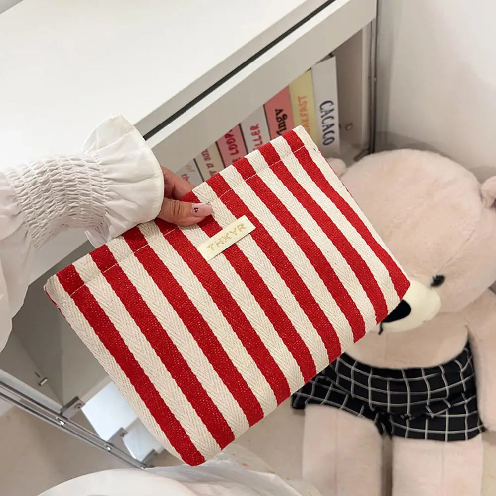 Un sac à main crochet rayé rouge et blanc tenu par une main à côté d'un grand ours en peluche rose.