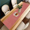 A light wood table is set with a red and white gingham table runner, plates, and a vase of greenery.